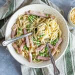 Creamy pasta dish with ham, green peas, and cheese served in a rustic bowl on a grey textured surface.