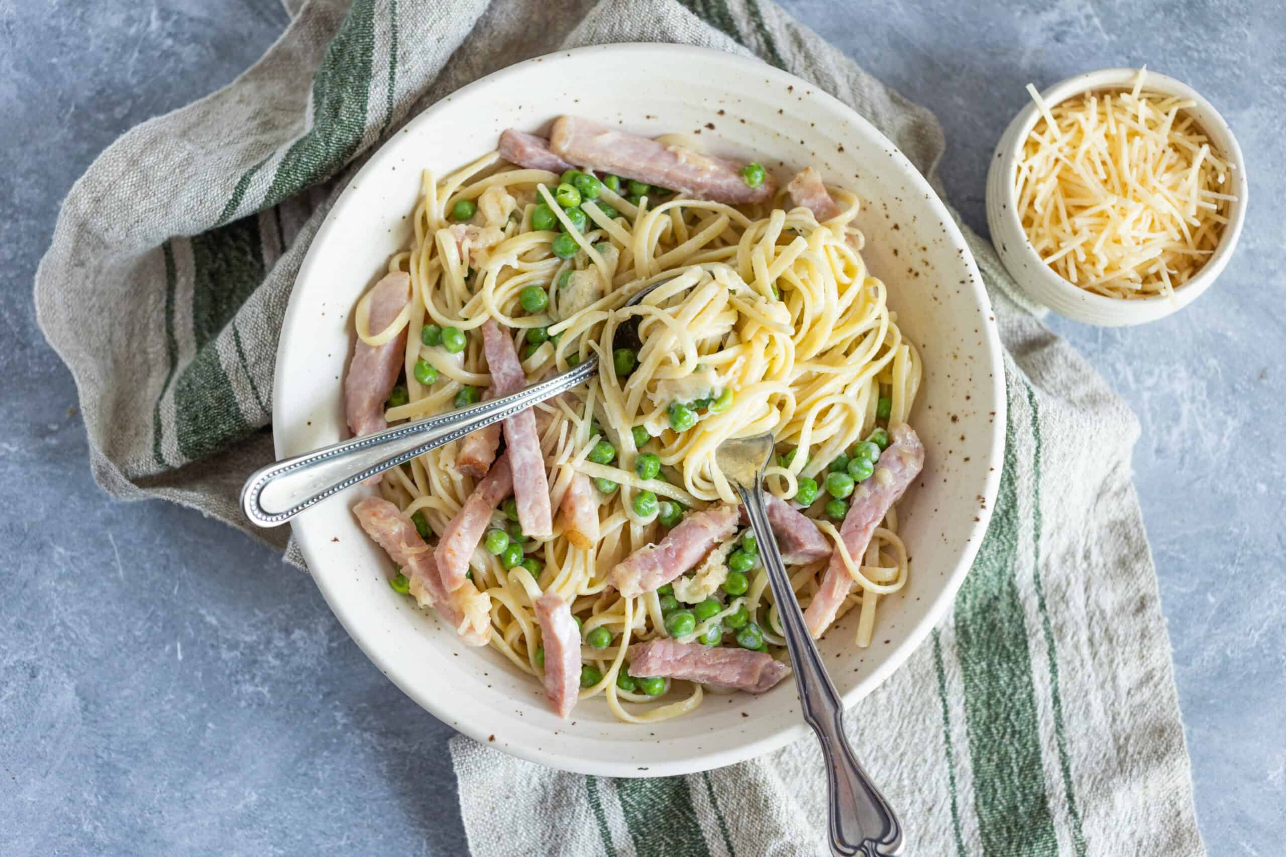 Creamy pasta dish with ham, green peas, and cheese served in a rustic bowl on a grey textured surface.