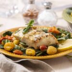 Fish fillet with roasted cherry tomatoes, spinach, and lemon slices on a yellow plate for a healthy dinner or lunch. Fresh ingredients, Mediterranean-inspired cuisine, and simple cooking style.