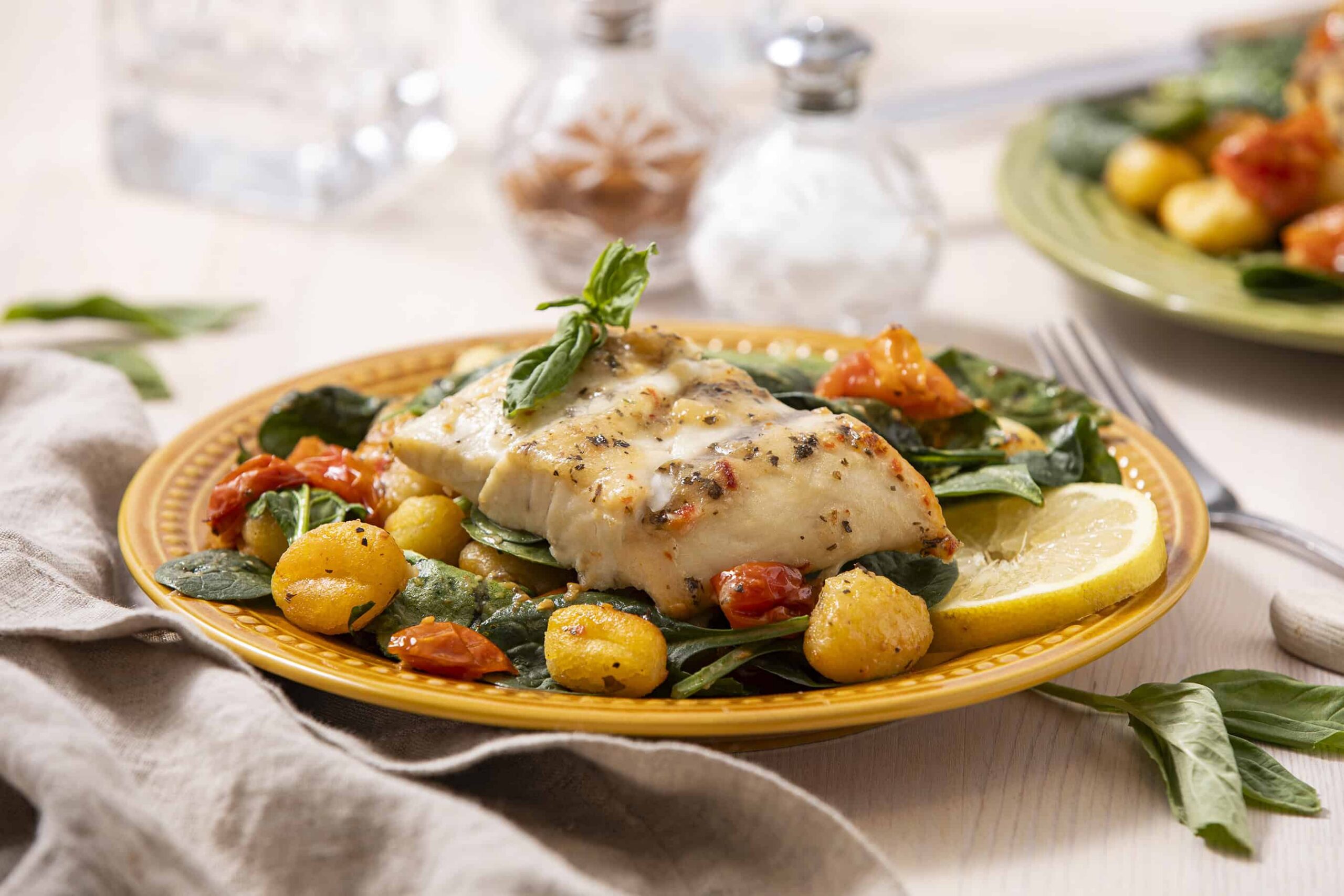 Fish fillet with roasted cherry tomatoes, spinach, and lemon slices on a yellow plate for a healthy dinner or lunch. Fresh ingredients, Mediterranean-inspired cuisine, and simple cooking style.