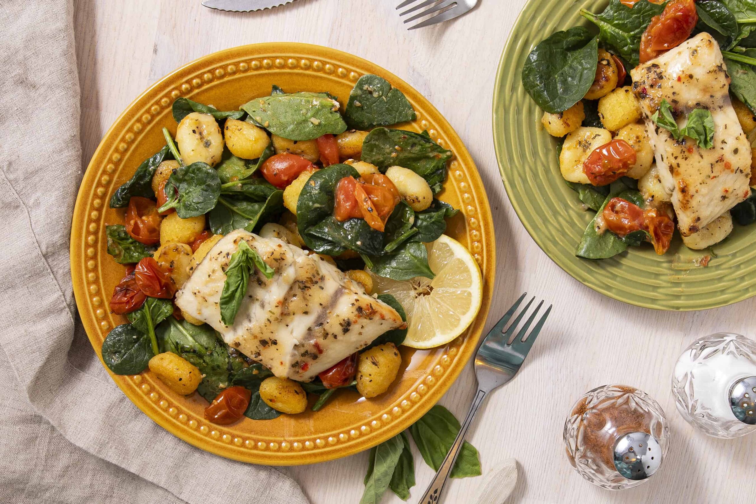Fresh baked fish with lemon, served with spinach, cherry tomatoes, and gnocchi on colorful ceramic plates, garnished with herbs for a flavorful, healthy meal.