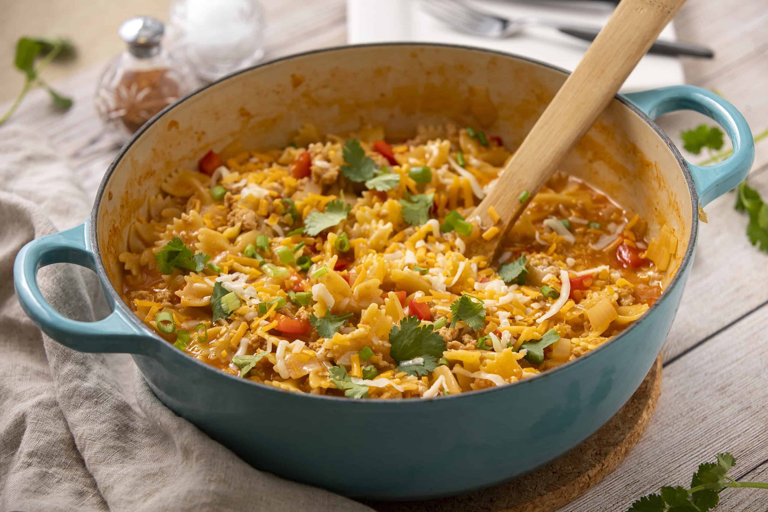 Creamy chicken and vegetable tortilla soup in a turquoise Dutch oven with fresh cilantro and shredded cheese garnishes.
