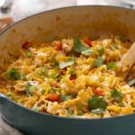 Creamy beef and cheese taco casserole in a turquoise skillet garnished with cilantro and green onions, served hot with melted cheese and flavorful seasonings.