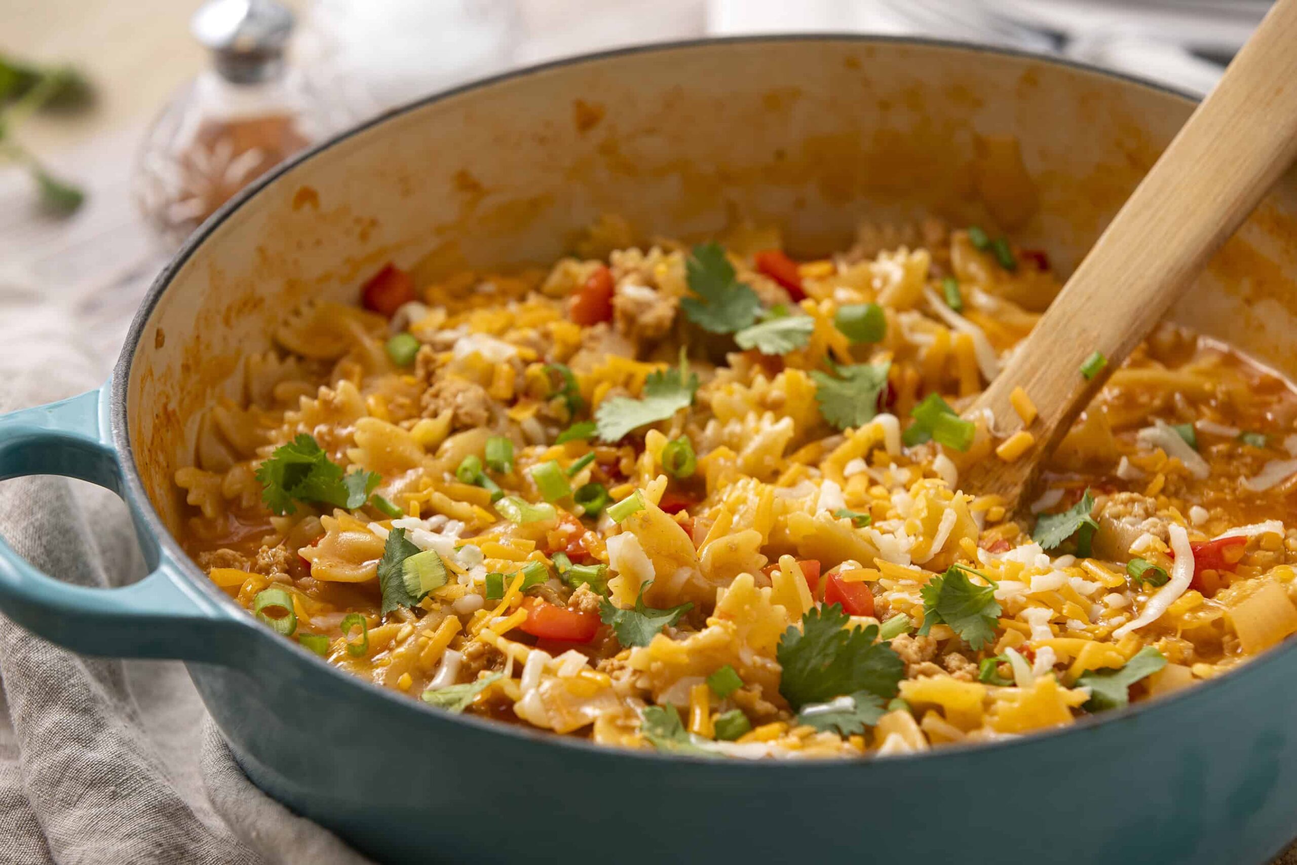 Creamy beef and cheese taco casserole in a turquoise skillet garnished with cilantro and green onions, served hot with melted cheese and flavorful seasonings.