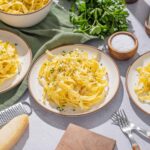 Creamy homemade fettuccine Alfredo with fresh parsley, served on rustic plates, with ingredients like Parmesan cheese, salt, and pasta on a kitchen countertop.