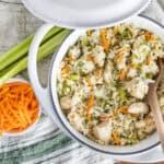 Creamy chicken fried rice with vegetables served in a white bowl, garnished with fresh herbs, surrounded by celery stalks, shredded carrots, and fresh cilantro for a flavorful Asian-inspired dish.