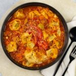 Hearty homemade tortellini soup in a rich tomato broth with vegetables and grated cheese, served in a black bowl, perfect for comforting meals and easy weeknight dinner ideas.