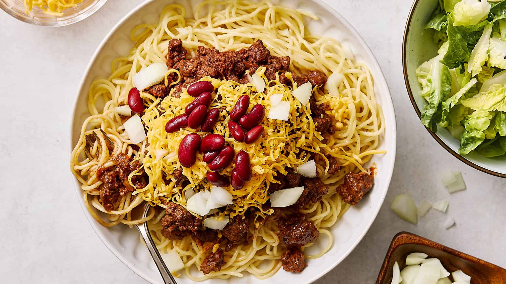 Tender spaghetti with seasoned ground beef, topped with shredded cheese, red bean, and chopped onions, served with fresh lettuce salad on the side. Perfect for a hearty, quick dinner.