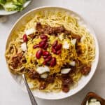 Savory beef spaghetti with kidney beans and shredded cheese on a white plate, topped with chopped onions, served with side bowls of shredded cheese and kidney beans, perfect for easy dinner recipes and comfort food.