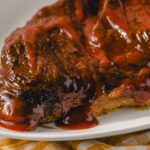 Juicy grilled steak topped with rich barbecue sauce on a white plate, perfect for a delicious beef dinner.