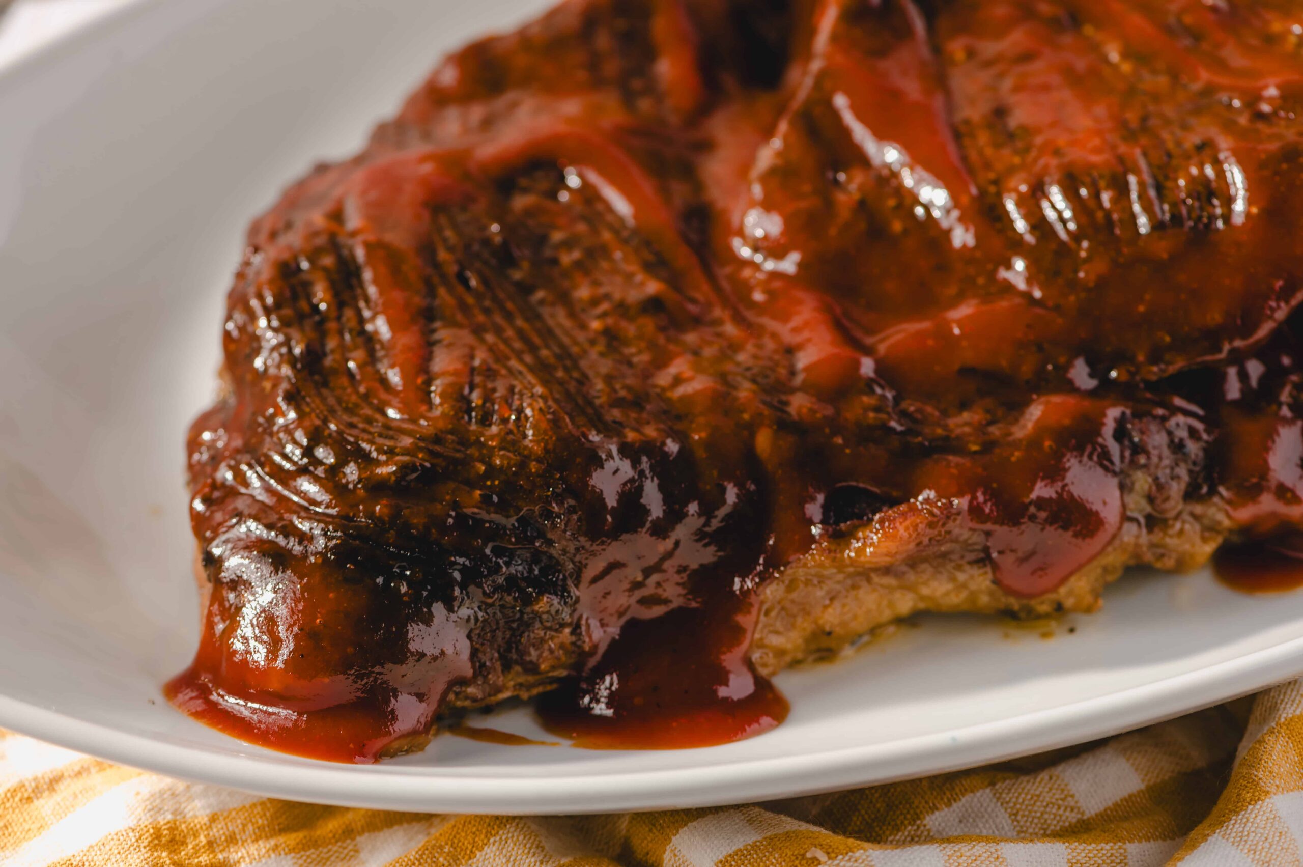 Juicy grilled steak topped with rich barbecue sauce on a white plate, perfect for a delicious beef dinner.