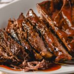 Slow-cooked barbecue ribs with rich, glossy sauce on a white serving dish, showcasing tender, flavorful meat ready to be enjoyed.