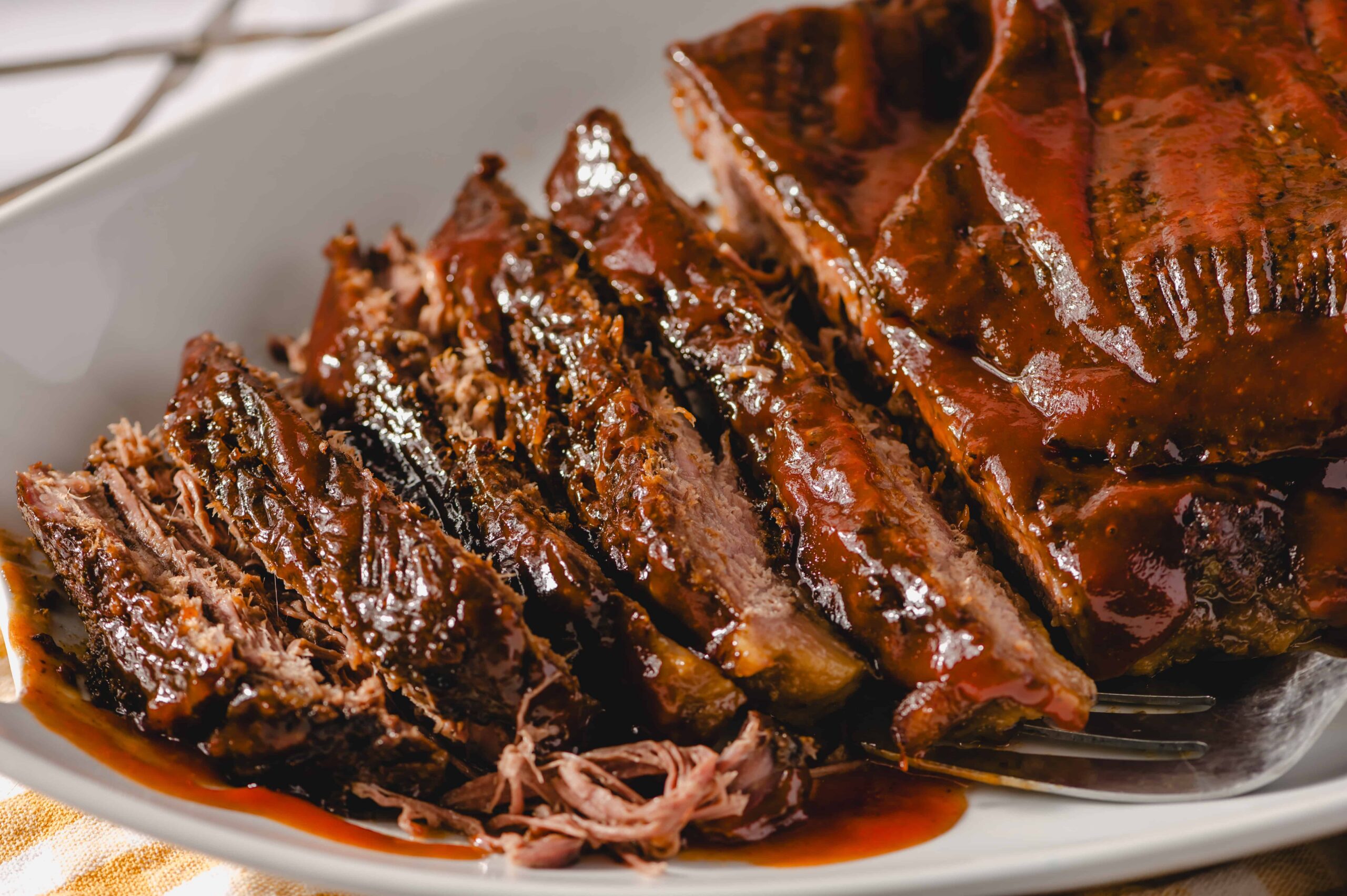 Slow-cooked barbecue ribs with rich, glossy sauce on a white serving dish, showcasing tender, flavorful meat ready to be enjoyed.