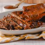 Slow-cooked barbecue ribs with rich, glossy sauce served in a white dish, ideal for family dinner, barbecue parties, and meat lovers. Perfectly cooked tender ribs with flavorful glaze.