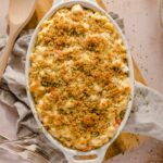 Creamy baked macaroni and cheese topped with golden breadcrumbs in a white oval dish, served on a rustic table with vintage forks, perfect comfort food.