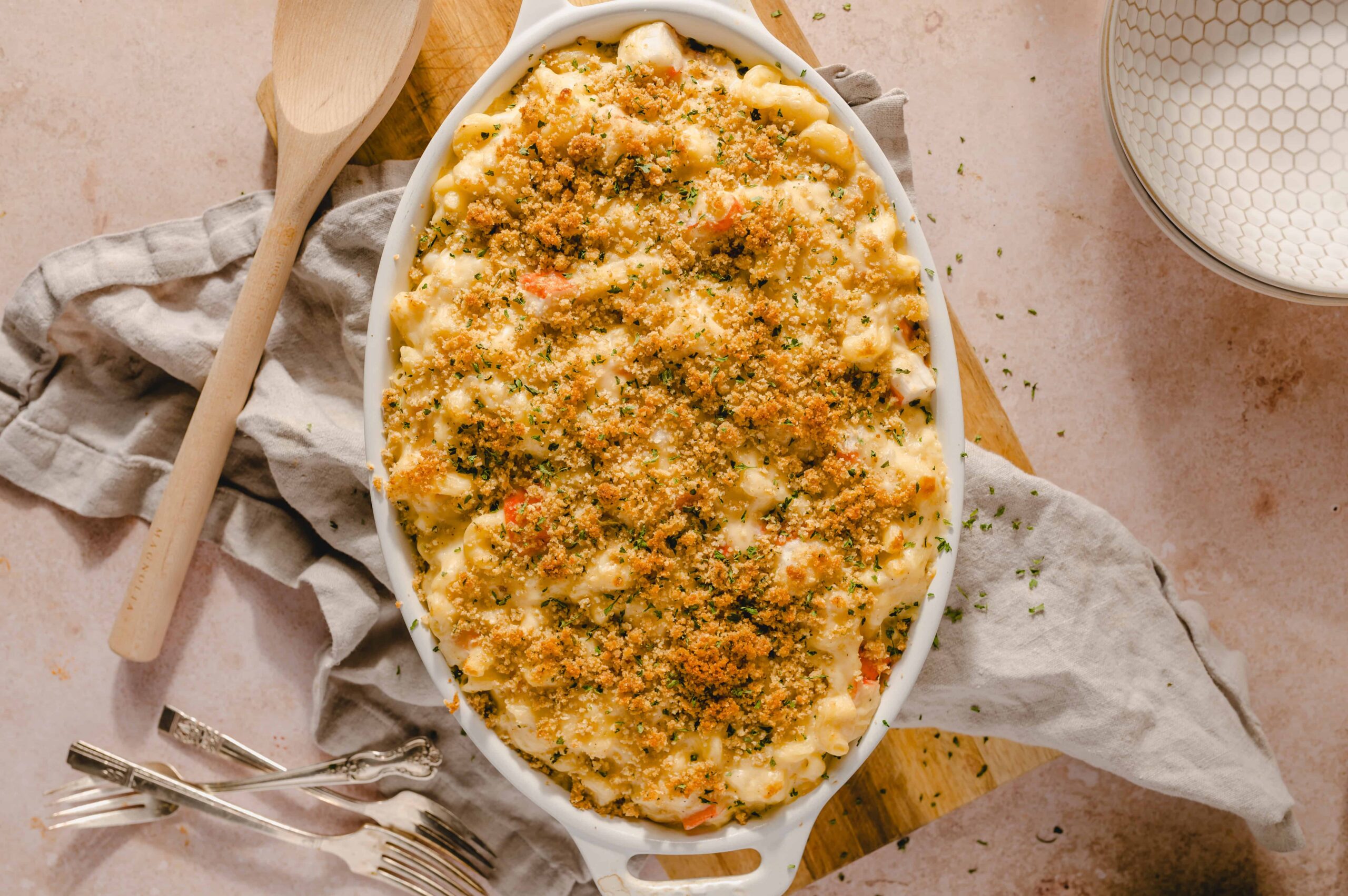 Creamy baked macaroni and cheese topped with golden breadcrumbs in a white oval dish, served on a rustic table with vintage forks, perfect comfort food.