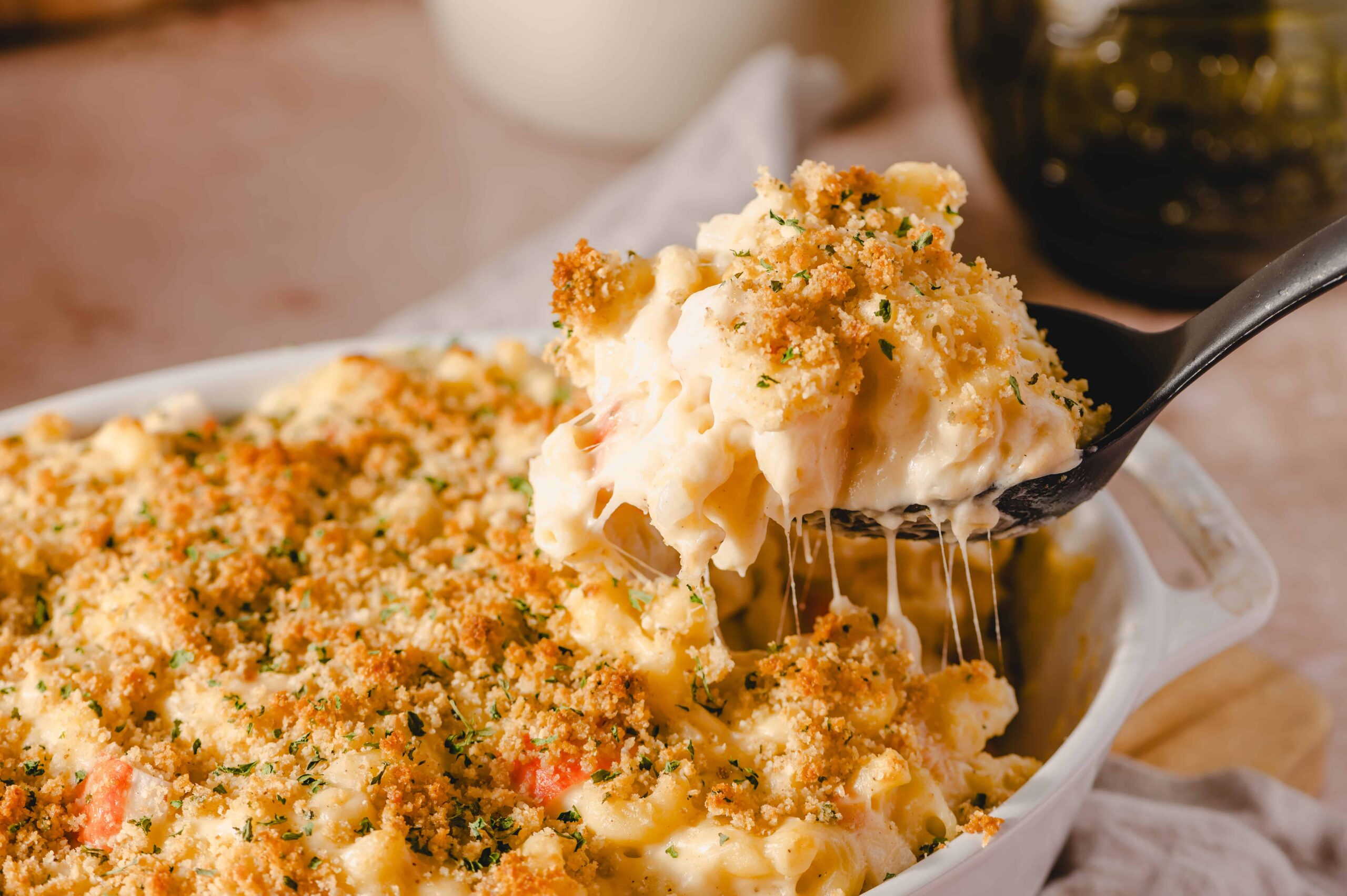 Creamy baked macaroni and cheese with a golden breadcrumb topping in a white ceramic dish, served hot with melted cheese pulling apart on a black spoon.