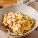 Creamy cauliflower casserole topped with breadcrumbs, garnished with herbs, served in a textured white bowl for a comforting vegetarian dish.