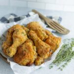 Golden crispy fried chicken drumsticks and thighs served on parchment paper with fresh herbs, perfect for a homemade comfort meal.