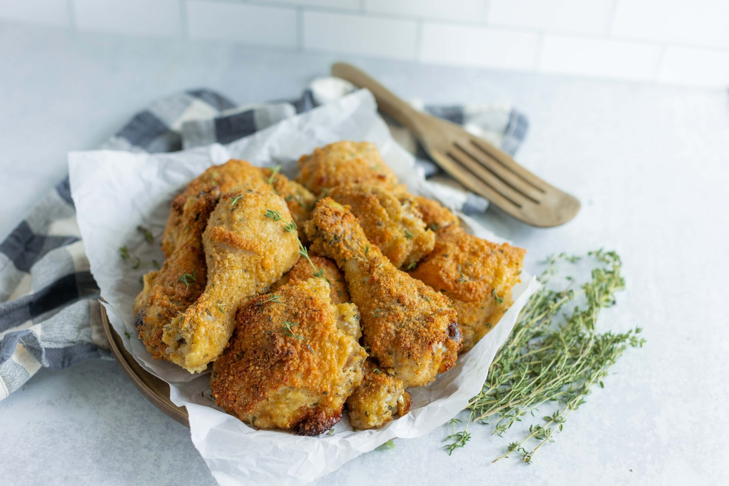 Golden crispy fried chicken drumsticks and thighs served on parchment paper with fresh herbs, perfect for a homemade comfort meal.