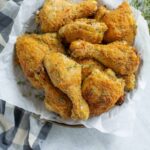 Crispy baked chicken drumsticks on parchment paper with fresh herbs, perfect for crispy fried chicken recipes and comfort food meals.