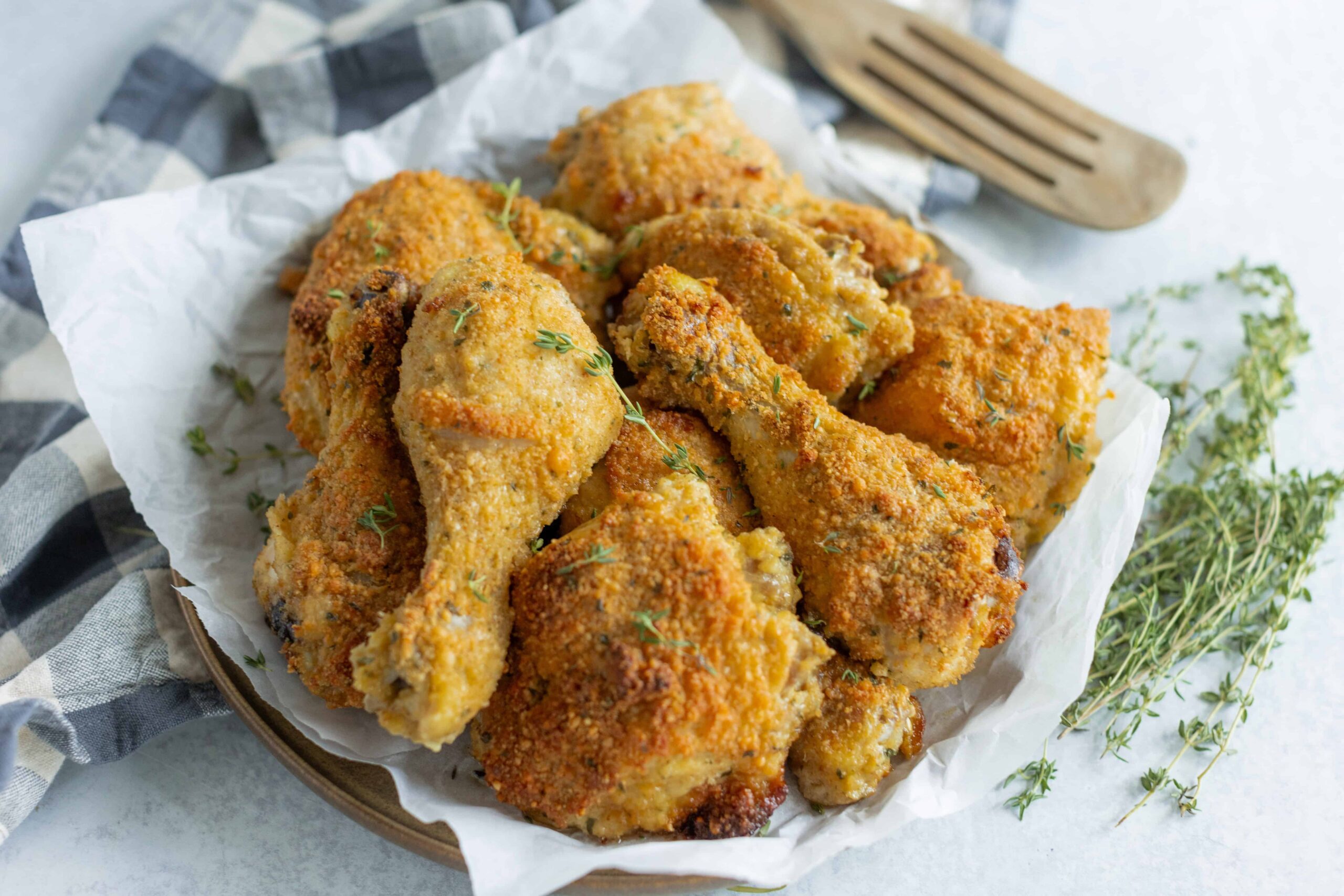 Crispy baked chicken drumsticks with golden breadcrumb coating, served on a piece of parchment paper with fresh thyme herbs. Perfect for a family dinner or casual outdoor meal.