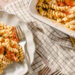 Creamy baked rotini pasta with tomatoes and herbs served on a white ceramic dish.