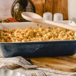 Creamy baked pasta casserole with rotini, cherry tomatoes, and herbs in a blue ceramic dish on a wooden cutting board, ready to serve.