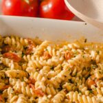 Fusilli pasta with cherry tomatoes, creamy cheese sauce, and chopped herbs in a white baking dish, served as a flavorful homemade Italian pasta bake.