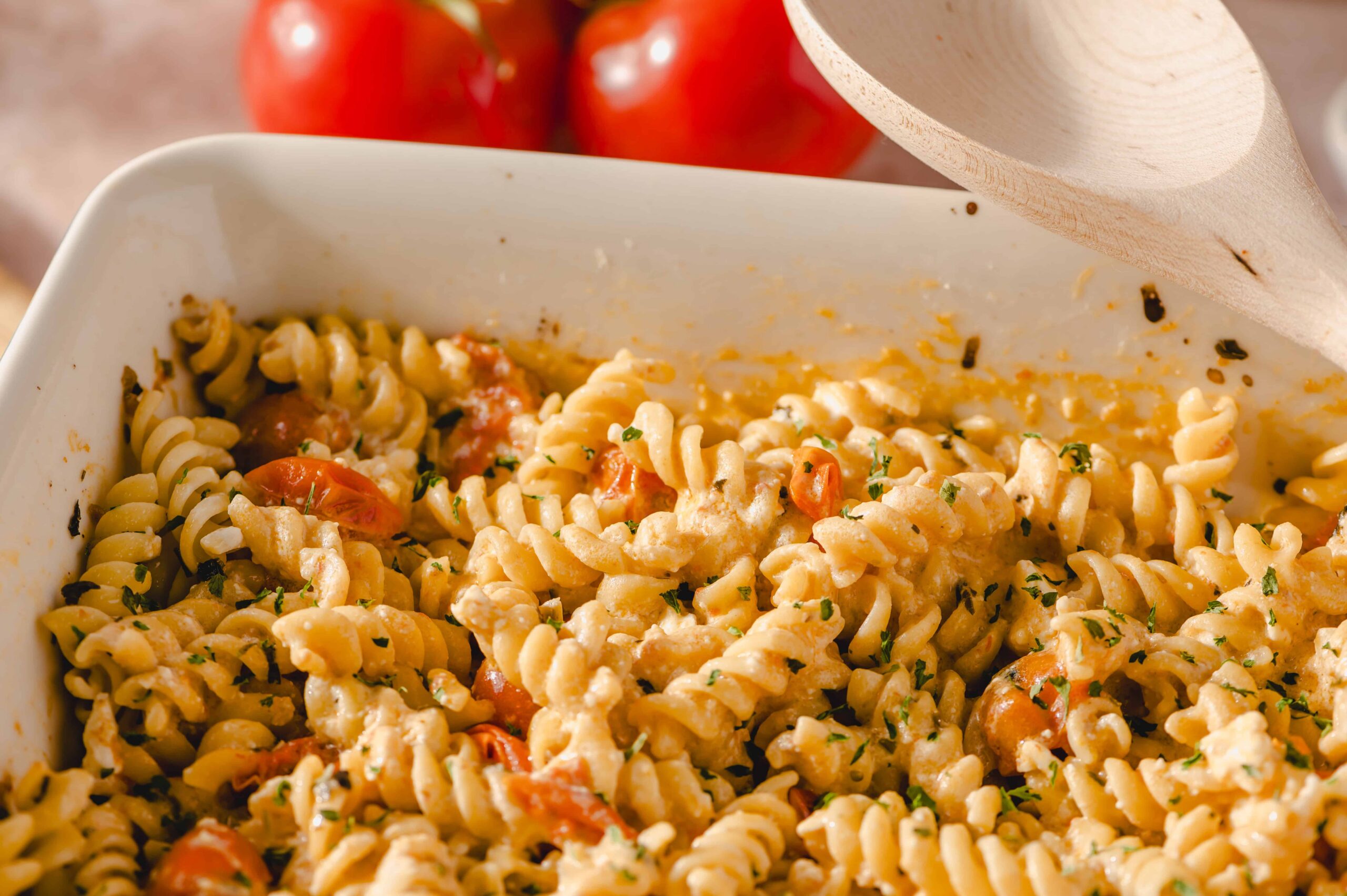 Fusilli pasta with cherry tomatoes, creamy cheese sauce, and chopped herbs in a white baking dish, served as a flavorful homemade Italian pasta bake.