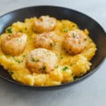 Savory chicken and herb meatballs served over creamy polenta garnished with fresh parsley in a black bowl. Perfect comfort food recipe for family dinner or special occasion.