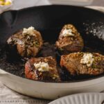 Succulent beef steaks cooked in a cast iron skillet topped with garlic butter and herbs, served for a delicious dinner or special occasion.