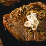 Juicy grilled steak topped with garlic herb butter on a sizzling hot cast iron skillet. Perfectly cooked and full of flavor, ideal for a delicious steak dinner.