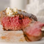 Juicy medium-rare steak topped with garlic herb butter on a white plate, showcasing perfect sear and tender interior. Ideal for steak lovers and dinner recipes.