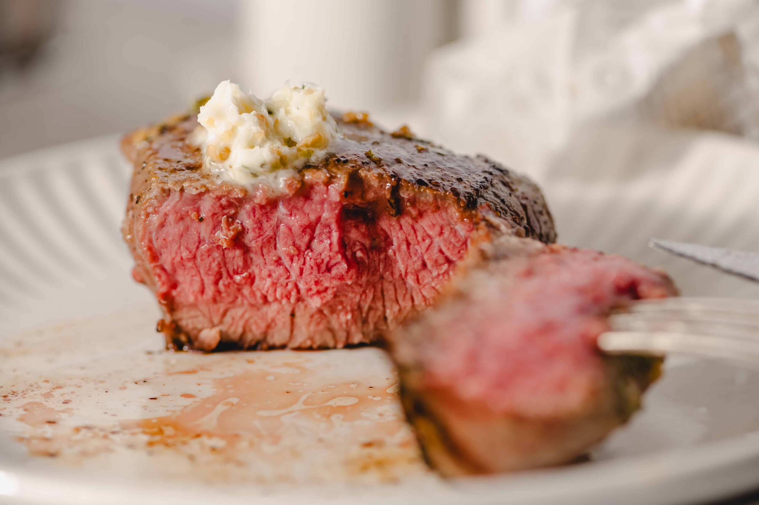 Juicy medium-rare steak topped with garlic herb butter on a white plate, showcasing perfect sear and tender interior. Ideal for steak lovers and dinner recipes.