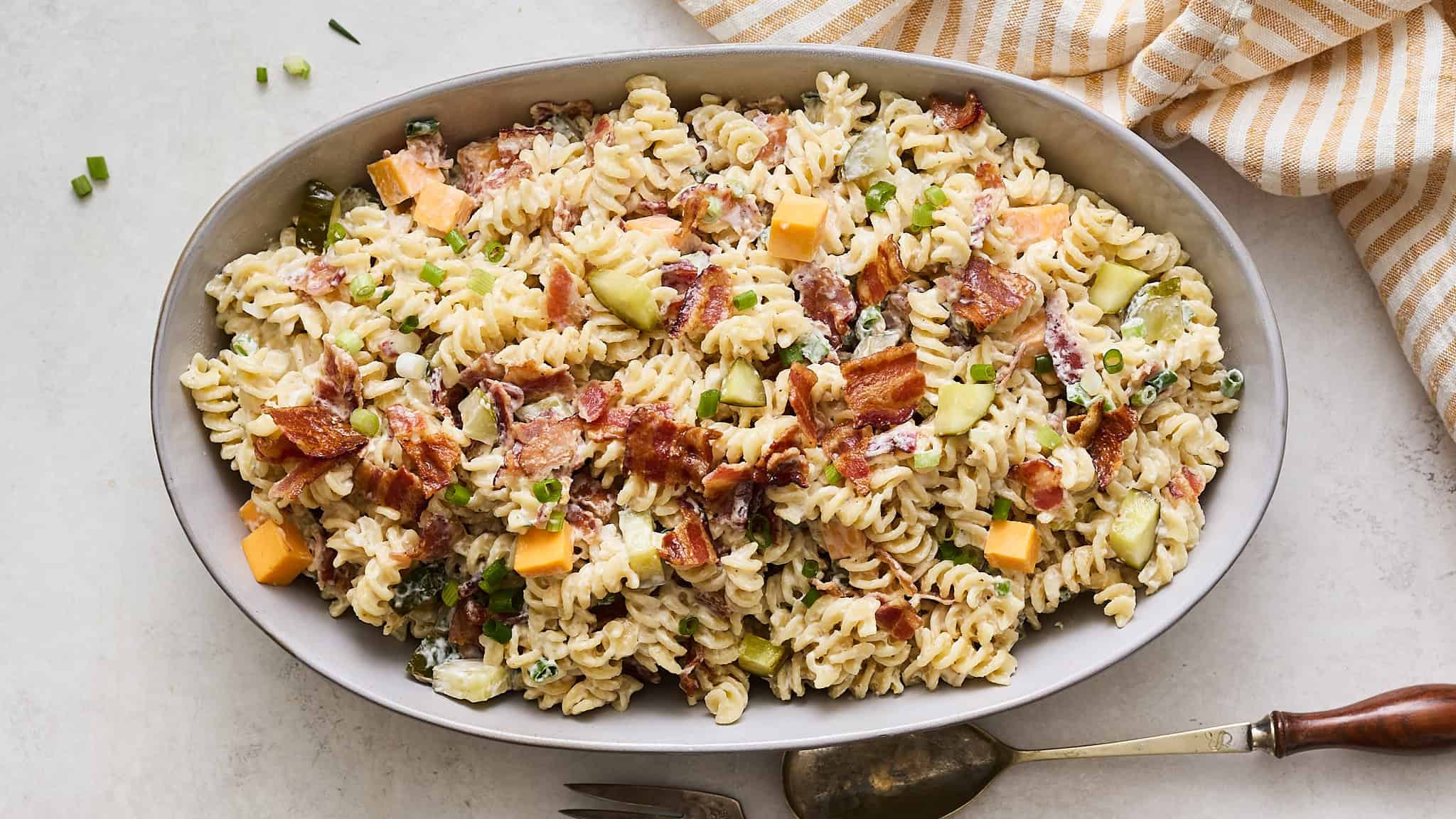 Creamy pasta salad with bacon, cheese, celery, and green onions in an oval serving dish. Fresh, flavorful, and perfect for a quick dinner or potluck.