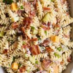 Creamy bacon and vegetable pasta casserole with rotini, cheddar, and green onions on a serving dish; close-up shot.
