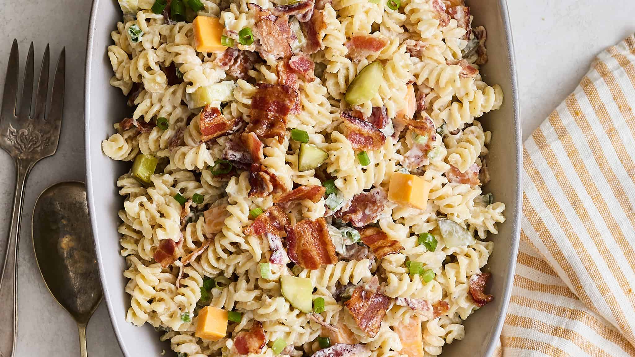 Creamy bacon and vegetable pasta casserole with rotini, cheddar, and green onions on a serving dish; close-up shot.