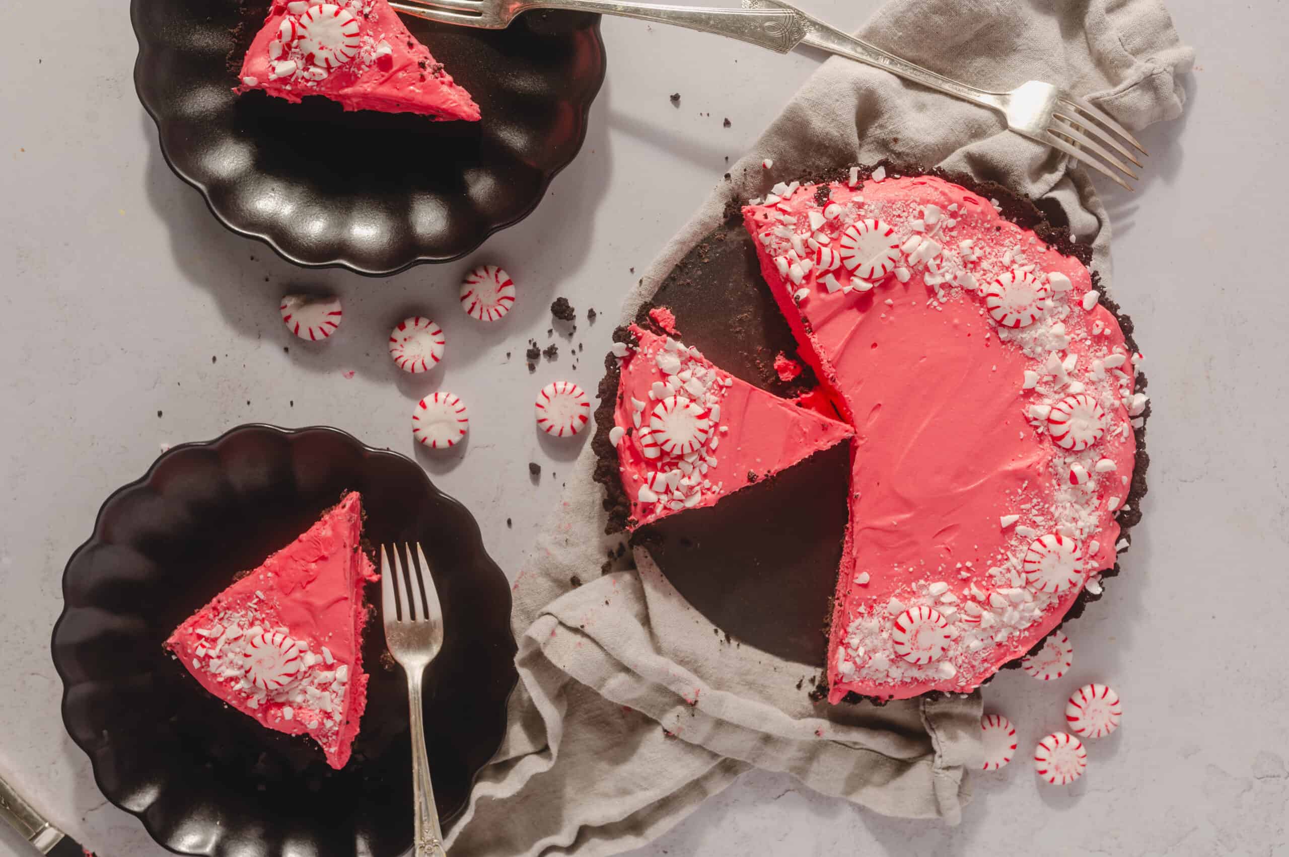 Sweet peppermint chocolate cake with pink icing and peppermint candies on top, presented on black plates for dessert, perfect for holiday celebrations, festive dessert ideas, Hey Recipe.