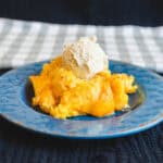Sweet peach cobbler topped with a scoop of vanilla ice cream on a decorative blue plate. Perfect for summer desserts and fruit-filled baked treats.