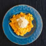 Creamy mashed pumpkin topped with a scoop of vanilla ice cream served on a vibrant blue plate, perfect for fall desserts or warm cozy treats.