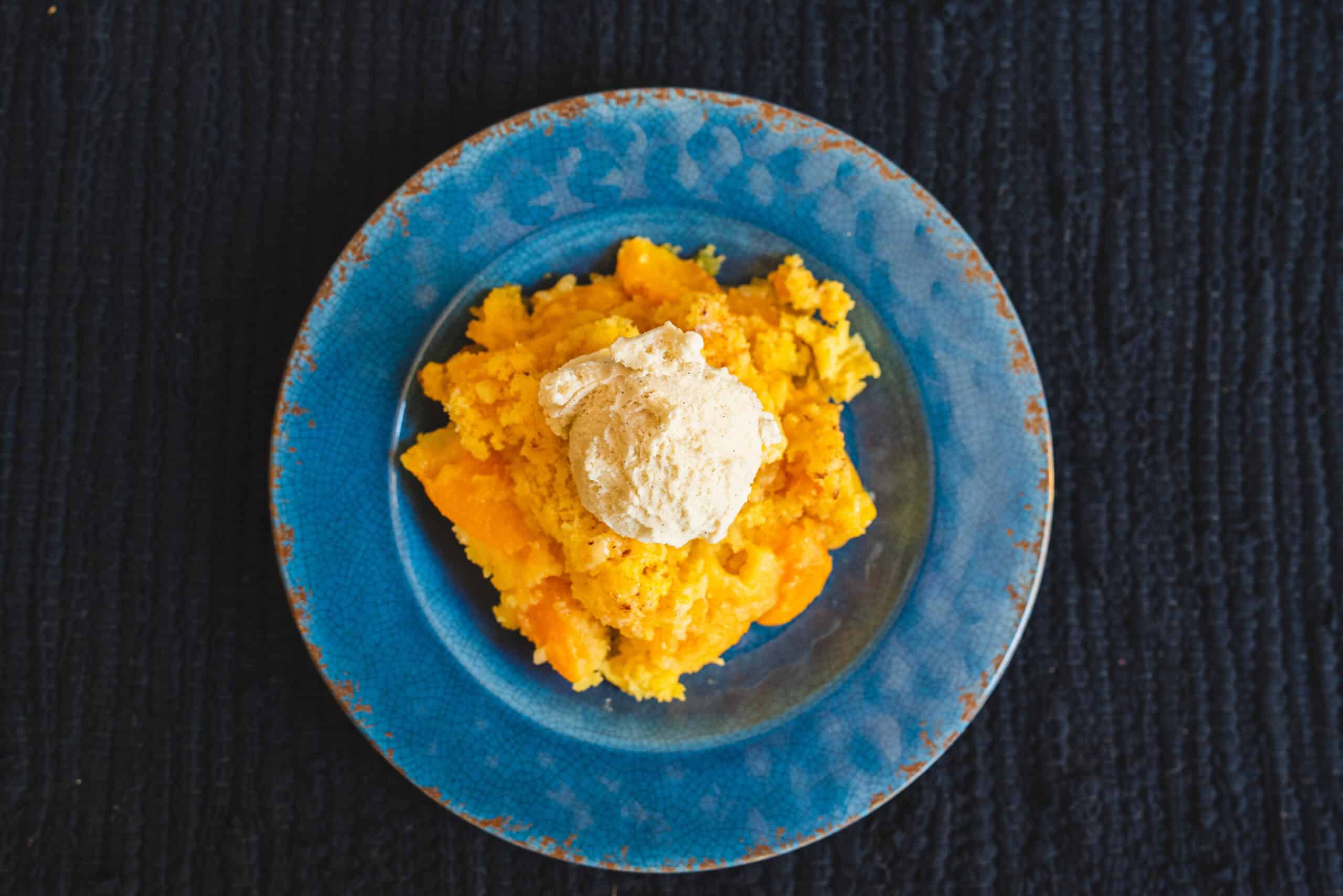 Creamy mashed pumpkin topped with a scoop of vanilla ice cream served on a vibrant blue plate, perfect for fall desserts or warm cozy treats.