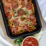 Cheeseburger spaghetti casserole topped with pepperoni and fresh herbs, served with a side of marinara sauce and shredded cheese, ready to bake for a delicious family meal.