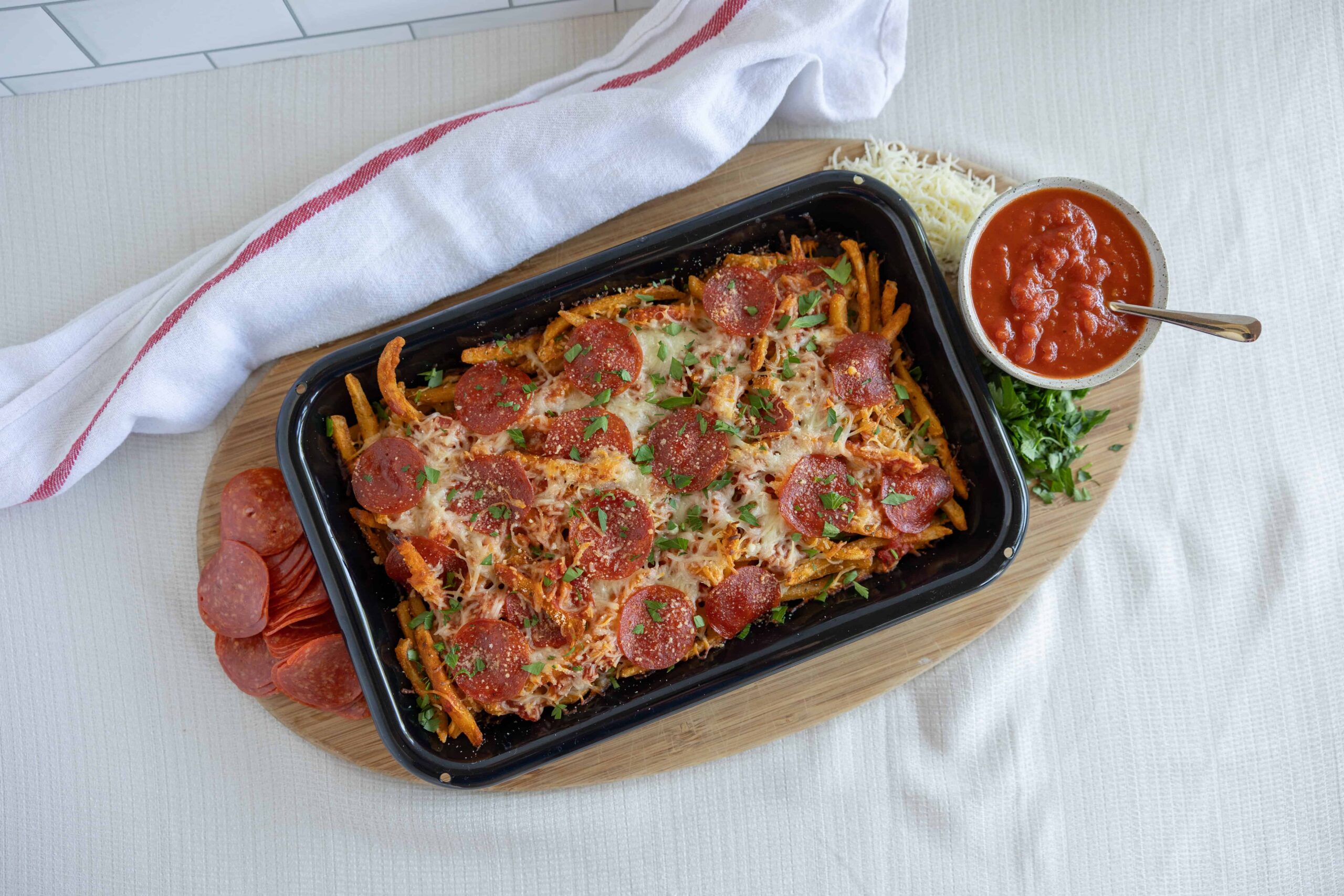 Slice pepperoni pizza with melted cheese, spaghetti, and tomato sauce served on a black tray with fresh herbs and shredded cheese on a wooden board.