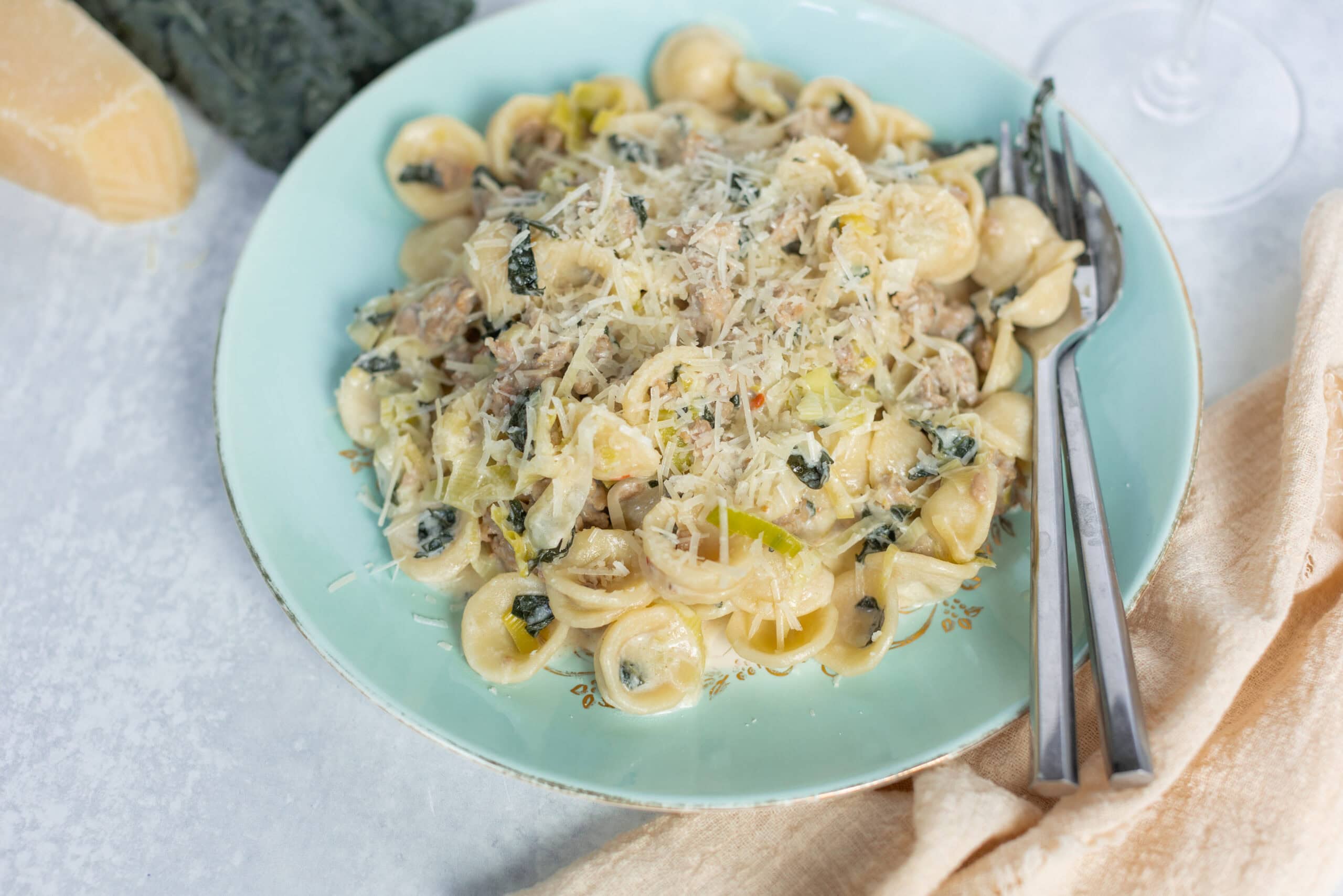 Creamy chicken and spinach tortellini pasta in a rich Alfredo sauce topped with grated parmesan cheese, served on a light blue plate with fresh ingredients in the background for a delicious homemade meal.