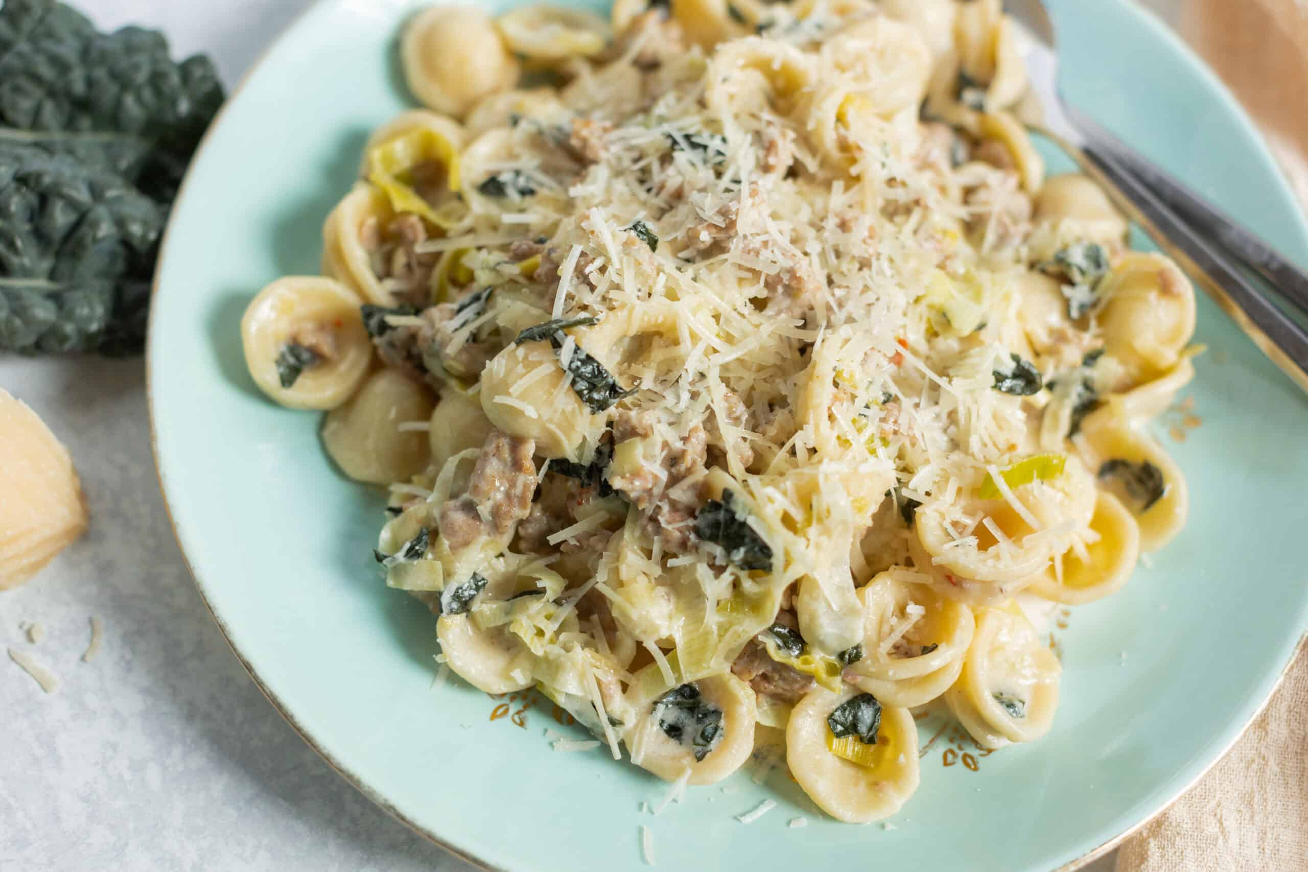 Creamy chicken and spinach tortellini pasta with grated Parmesan cheese served on a light green plate, featuring tender tortellini, sautéed spinach, and shredded chicken in a rich, cheesy sauce.