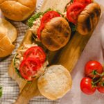 Fresh homemade chicken salad sandwiches with sliced tomatoes on toasted bread buns, served on a wooden cutting board with fresh tomatoes and lettuce for a healthy meal.