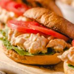 Creamy chicken salad sandwich with fresh tomatoes, lettuce, and a toasted bun on wooden serving board. Perfect for lunch or casual meal, featuring flavorful ingredients and crispy bread.