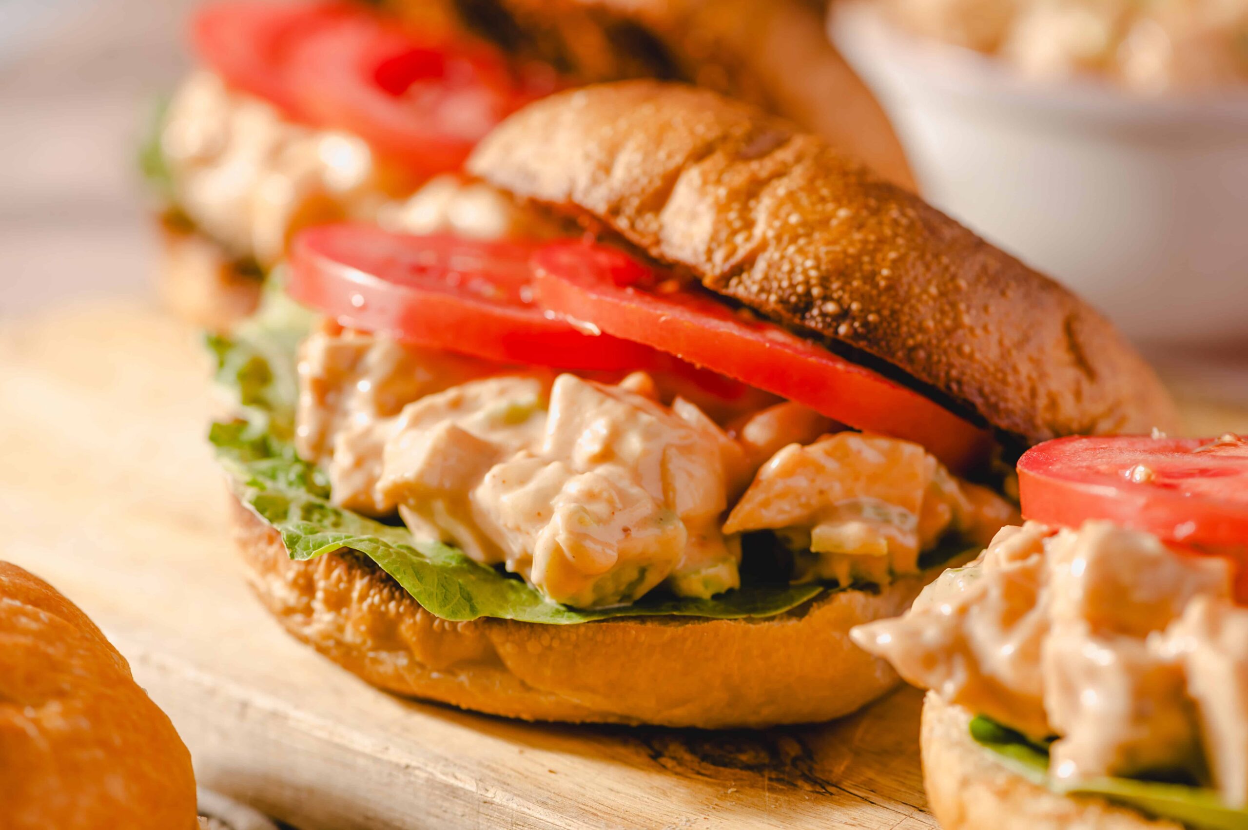 Creamy chicken salad sandwich with fresh tomatoes, lettuce, and a toasted bun on wooden serving board. Perfect for lunch or casual meal, featuring flavorful ingredients and crispy bread.