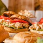 Creamy chicken salad sandwich with fresh lettuce and tomato on toasted bread, served with side bread rolls; ideal for easy lunch recipes and delicious sandwich ideas.